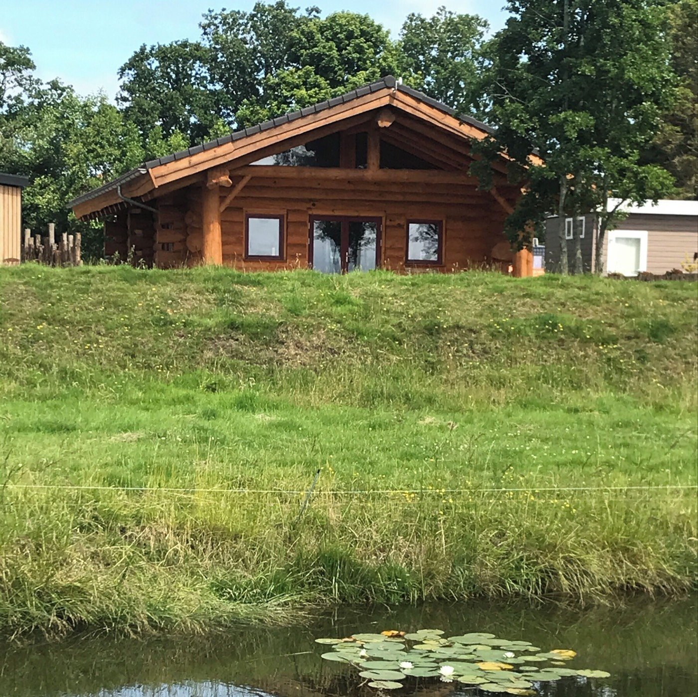 Het afgebouwde huis, gezien over het gras en de vijver